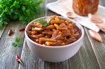 Tomato lobio of green bean pods in a bowl on a wooden background. Lenten dish.
