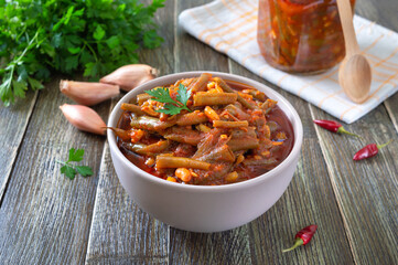 Tomato lobio of green bean pods in a bowl on a wooden background. Lenten dish.
