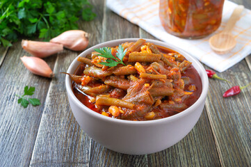 Tomato lobio of green bean pods in a bowl on a wooden background.   Lenten dish.