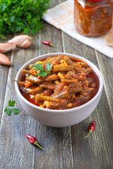Tomato lobio of green bean pods in a bowl on a wooden background. Lenten dish.