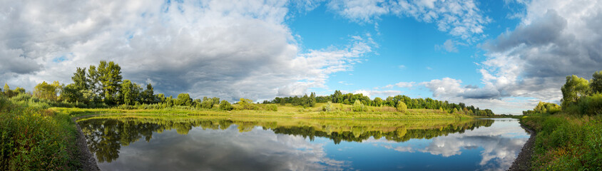 Summer panoramic landscape with calm river and beautiful clouds in blue sky