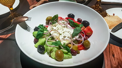 Greek salad of cucumbers, tomatoes, olives and feta cheese is on the plate.