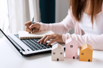 Closeup of a happy young Asian woman searching home information online with a laptop and writing on...