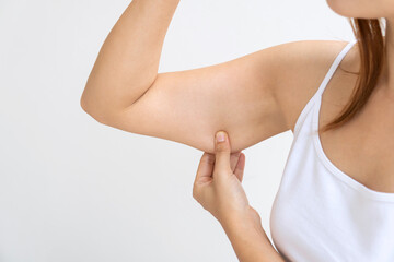 Young Asian woman pinching loose skin or flab on her upper arm - obrazy, fototapety, plakaty