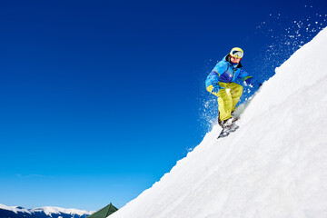 Male snowboarder riding snowboard fast down steep snowy mountain slope, jumping in air on copy...