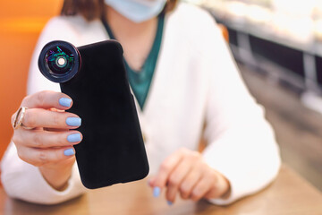 Young woman holds smartphone in a black case with extra lens. Indoor shot.