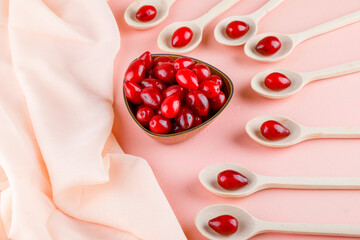 Cornel berries in wooden spoons and bowl on pink and textile background. high angle view.