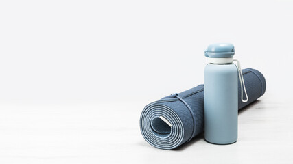 Rolled blue yoga mat and blue water bottle on grey wooden surface. Gender neutral fitness yoga and...