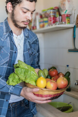 Young man with basket with vegetables in the kitchen. Casual young man with a beard.