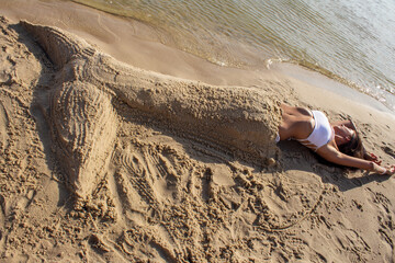 sand figure with a mermaid tail of a girl in a white swimsuit on the seashore