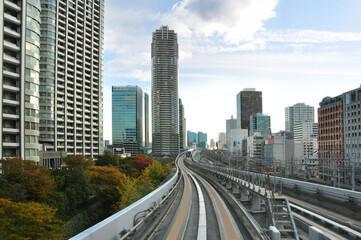 Fototapeta premium Riding on monorail train to Odaiba Island among modern and Futuristic architecture of Tokyo city and autumn color trees