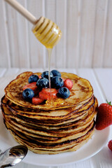 Close-up delicious pancakes, with fresh blueberries, strawberries and maple syrup on a light background. With copy space. Pile of small homemade pancakes with forest fruits.