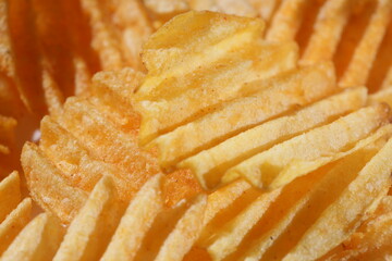 Background corrugated golden chips with texture. Potato chips is snack, ready to eat and fat food or junk food. Horizontal. Top view.