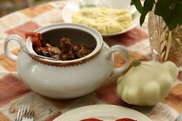 country outdoor still life with tureen with roasted meat, patisson, mashed potato on the table close up photo