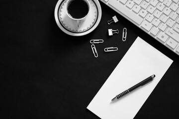 Creative flat lay, remote work concept, black and white photo of workspace desk with computer keyboard, pen, notepad, coffee and paper clips, a free copy space,  minimal style, selective focus