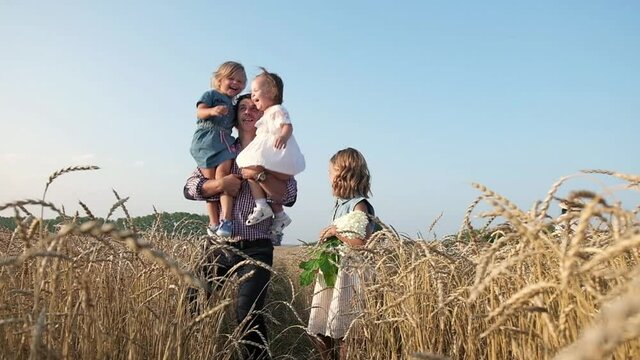 happy father walks through wheat field with his three daughters. man holds the girls on his shoulders throws them up and children laugh. Walk through field in summer with family and children.