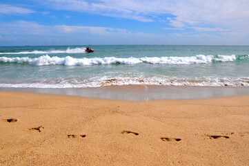 Watercraft riding on the waves with human footprints on the sand at the foreground on the sunny day at the Haeundae beach, Busan, South Korea