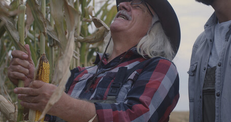 Cheerful elderly farmer showing corn to grandson