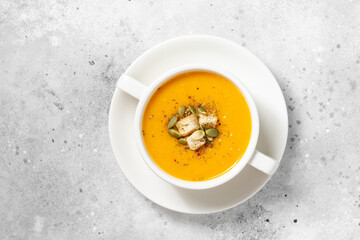 Pumpkin soup. Pumpkin cream soup in a white plate on the light gray kitchen table. Vegetarian autumn soup close-up. The view from the top