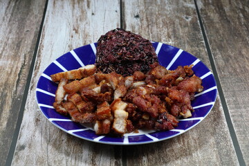 Steamed sticky brown rice serving with chopped deep fried pork belly on the plate. Famous traditional breakfast menu in Asia. 