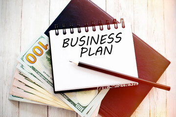 BUSINESS PLAN text written on notebook with dollar bills and pencil