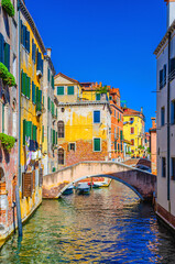 Venice cityscape with narrow water canal with boats moored between old colorful buildings and stone bridge, Veneto Region, Northern Italy. Typical Venetian view, vertical view, blue sky background