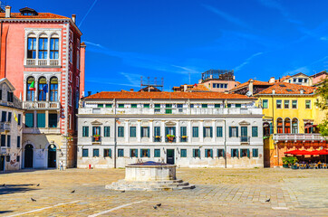 Fototapeta premium Palace buildings and stone well on Campo San Polo square in Venice historical city centre, blue sky background in summer day, Veneto Region, Northern Italy