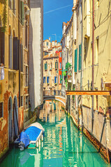 Venice cityscape with narrow water canal with colorful boats moored near old multicolored buildings, Veneto Region, Northern Italy. Typical Venetian view, vertical view, blue sky background