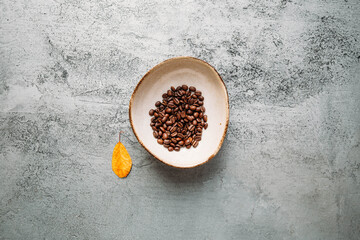 Autumn concept with coffee beans and yellow leaf on concrete background with copy space