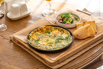 Omelet in a frying pan with parsley and dill. Serve with fresh bread and fresh vegetables.