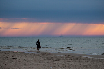 Piękny zachód słońca nad morzem. Na horyzoncie widać jak pada deszcz. Człowiek patrzy na zachód słońca. © Anastasiia