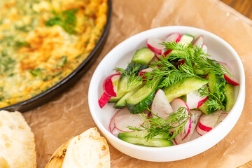 Omelet in a frying pan with parsley and dill. Serve with fresh bread and fresh vegetables.
