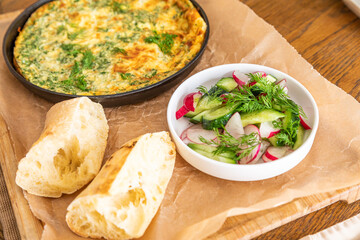 Omelet in a frying pan with parsley and dill. Serve with fresh bread and fresh vegetables.