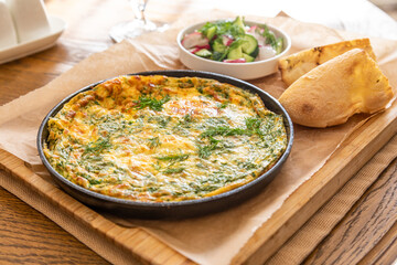 Omelet in a frying pan with parsley and dill. Serve with fresh bread and fresh vegetables.