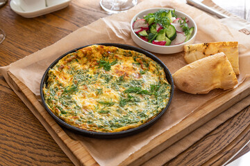 Omelet in a frying pan with parsley and dill. Serve with fresh bread and fresh vegetables.