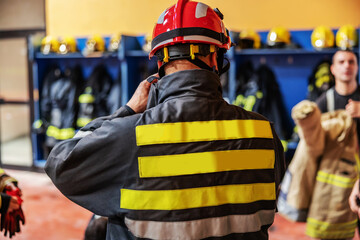 Fototapeta premium Rear view of firefighter putting on his protective clothes na d helmet while standing in fire brigade.