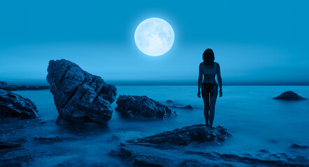 Silhouette of a beautiful girl standing on the beach, full moon in the background "Elements of this image furnished by NASA "