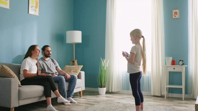 Small blonde girl plays interesting game with parents using gadget, explains words by paraphrasing, use gestures, does her best to succeed in the game, live family communication, Slow motion.