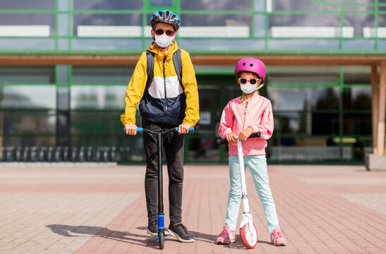 Education, Childhood And People Concept - School Children In Face Protective Medical Mask For Protection From Virus Disease Riding Scooters Outdoors