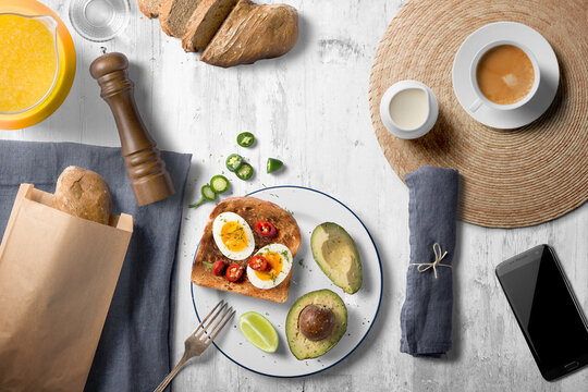 Top view breakfast scene with egg on toast, avocado and peppers, orange juice, coffee and sliced fresh bread on a whitewashed wooden counter