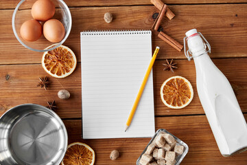 cooking, christmas and seasonal drinks concept - notebook with pencil, ingredients for eggnog, pot...