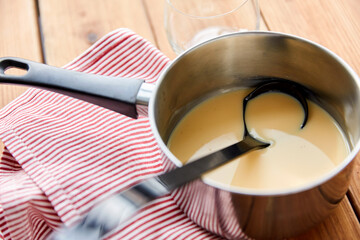 christmas and seasonal drinks concept - pot with eggnog and ladle with kitchen towel on wooden background