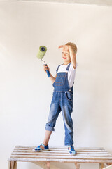 a blond child stands on a construction ladder in an apartment with white walls and a roller in his hands and looks into the distance, a place for text, the concept of repair