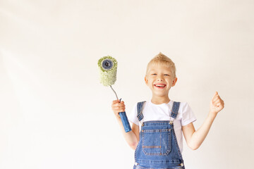 a child Builder in an apartment with white walls and a roller in his hands shows the class, a place for text, the concept of repair