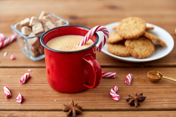 Obraz na płótnie Canvas christmas and seasonal drinks concept - red cup of eggnog with candy cane, oatmeal cookies, star anise and cinnamon on wooden background