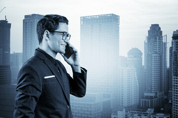 Fototapeta na wymiar Prosperous handsome entrepreneur in suit and glasses pensively talking phone and looking on Bangkok cityscape. The concept of problem solving consulting. Downtown view. Double exposure.