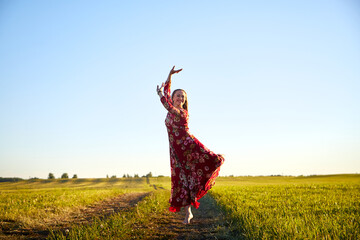 Beautiful woman or girl with magnificent figure and plastic movements walking and dancing in green field with trimmed grass in the setting sun during sunset with warm yellow light.