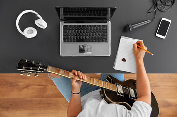 leisure and people concept - young man or musician with laptop computer and guitar writing to music...