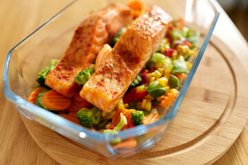 food, eating and culinary concept - close up of salmon fish with vegetables in baking dish on kitchen table at home