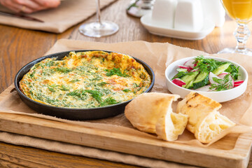 Omelet in a frying pan with parsley and dill. Serve with fresh bread and fresh vegetables.